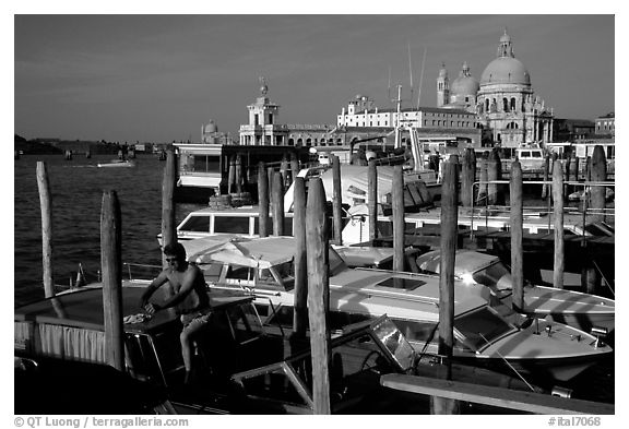 Water taxi driver cleaning out his boat in the morning, Santa Maria della Salute in the background. Venice, Veneto, Italy (black and white)