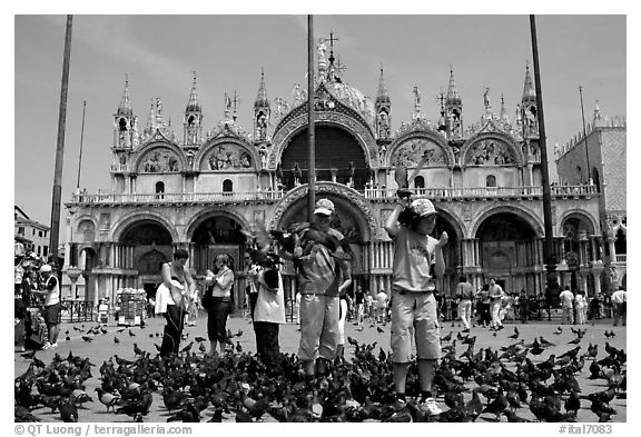 Children feeding flock of pigeon, in front of the Basilica San Marco, mid-day. Venice, Veneto, Italy
