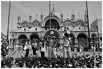 Children feeding flock of pigeon, in front of the Basilica San Marco, mid-day. Venice, Veneto, Italy (black and white)