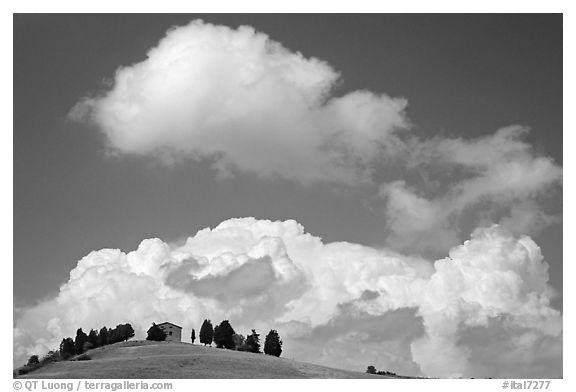 Fluffy clouds above ridge with cypress trees and house. Tuscany, Italy (black and white)