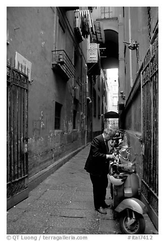 Man locking his motorbike in a side street. Naples, Campania, Italy (black and white)