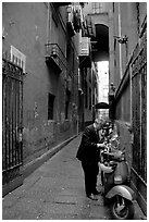 Man locking his motorbike in a side street. Naples, Campania, Italy ( black and white)