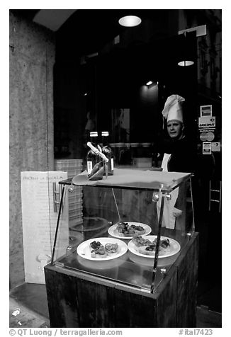 Chef at restaurant doorway with appetizers shown in glass case. Naples, Campania, Italy (black and white)