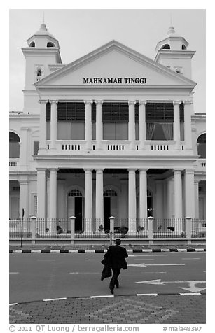 Man in suit crossing streets towards court building. George Town, Penang, Malaysia (black and white)