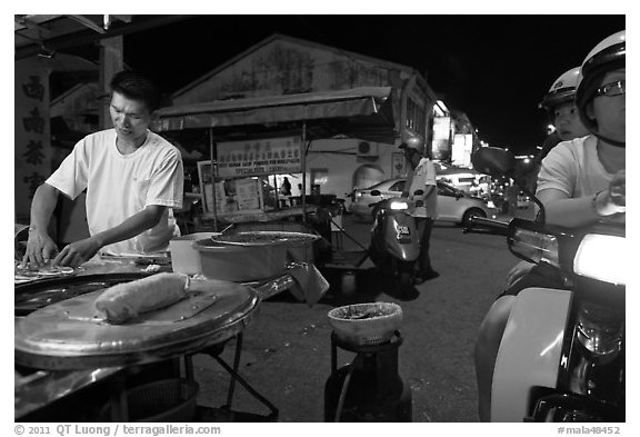 Man preparing food as people wait on motorbike. George Town, Penang, Malaysia (black and white)