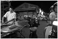 Man preparing food as people wait on motorbike. George Town, Penang, Malaysia (black and white)