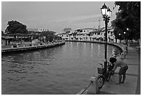 Woman locking bicyle on quay of Melaka River. Malacca City, Malaysia (black and white)