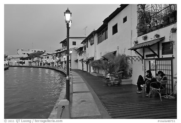 Women relaxing in front of riverside house, dusk. Malacca City, Malaysia (black and white)