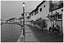 Women relaxing in front of riverside house, dusk. Malacca City, Malaysia (black and white)