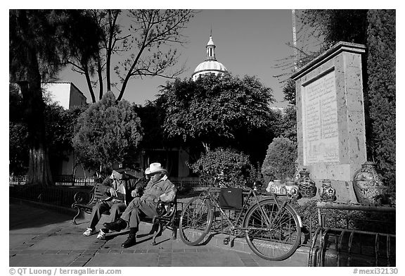 Men sitting in garden, with cathedral dome and ceramic monument, Tlaquepaque. Jalisco, Mexico (black and white)