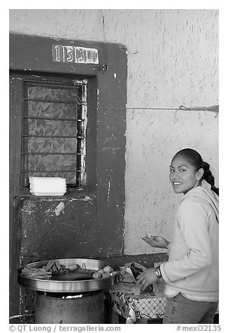 Woman preparing food outside a blue wall, Tonala. Jalisco, Mexico (black and white)