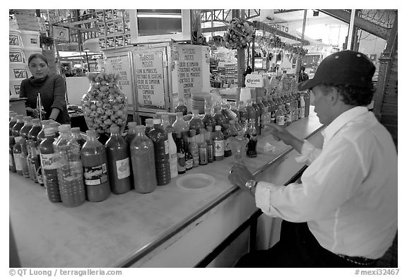 Man sitting at a booth offering a large variety of bottled chili. Guanajuato, Mexico (black and white)