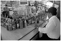 Man sitting at a booth offering a large variety of bottled chili. Guanajuato, Mexico ( black and white)