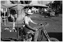 Man with cigarette riding a motorcycle-powered food stand on town plaza. Mexico (black and white)