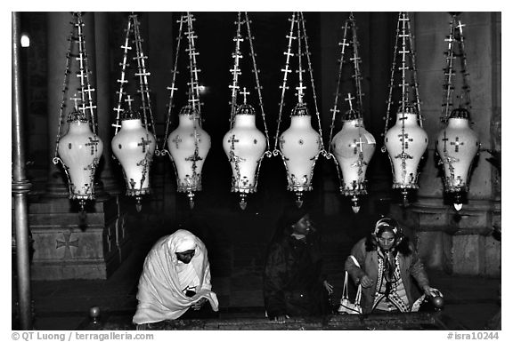 Women worshiping beneath hanging lamps inside the Church of the Holy Sepulchre. Jerusalem, Israel