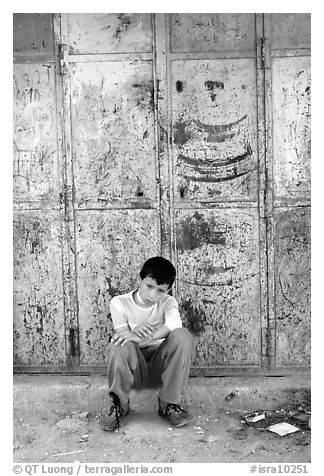 Young boy sitting in front of a closed store, Hebron. West Bank, Occupied Territories (Israel)