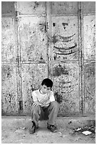 Young boy sitting in front of a closed store, Hebron. West Bank, Occupied Territories (Israel) (black and white)