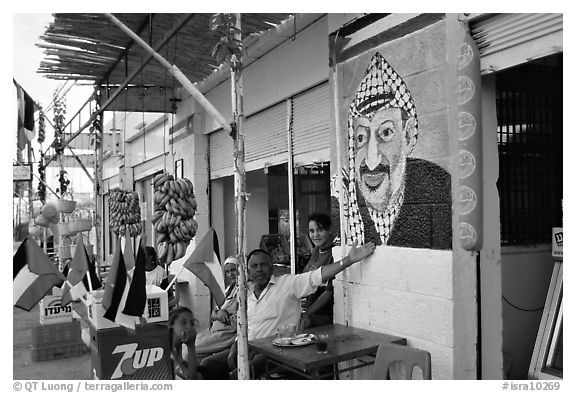 Palestinian cafe owner pointing proudly to a painting of Yasser Arafat, Jericho. West Bank, Occupied Territories (Israel) (black and white)