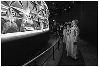 Visitors in Arab dress looking at curved wall of stars with projected media, USA Pavilion. Expo 2020, Dubai, United Arab Emirates ( black and white)