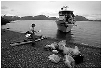 Kayaker standing with gear wrapped in plastic bags after drop-off. Glacier Bay National Park, Alaska (black and white)