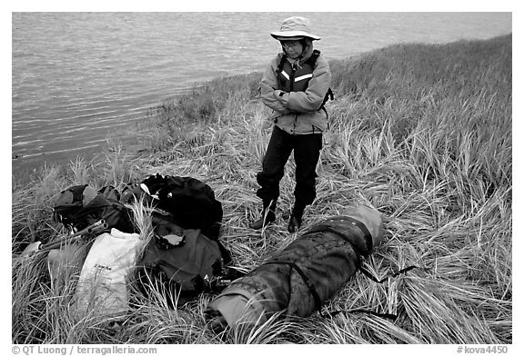 Canoeist standing next to gear and deflated and folded  canoe. Kobuk Valley National Park, Alaska