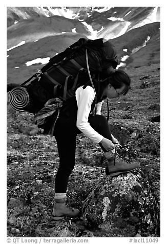 Woman backpacker with a large backpack tying up her shoelaces. Lake Clark National Park, Alaska