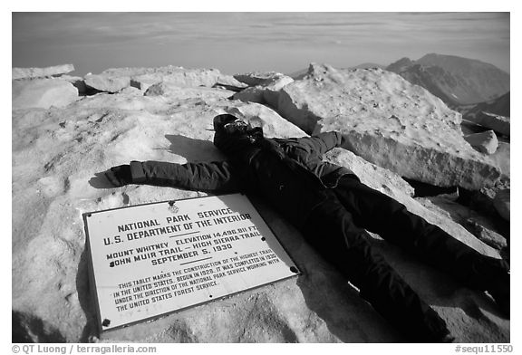 Hiker laying exhausted on Mt Whitney summit sign. Sequoia National Park, California