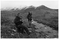 Backpackers eating by a creek and snowy mountains. Gates of the Arctic National Park ( black and white)