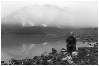 Backpacker eating near lake with foggy mountain. Gates of the Arctic National Park ( black and white)
