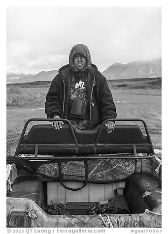 Nuamiunt boy standing on all-terrain vehicle, Anaktuvuk Pass Airport. Gates of the Arctic National Park (black and white)