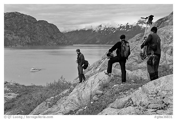 Film crew carrying a motion picture camera down rocky slopes. Glacier Bay National Park (black and white)