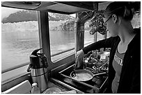 Woman cooking eggs aboard small tour boat, with glacier in view. Glacier Bay National Park, Alaska, USA. (black and white)