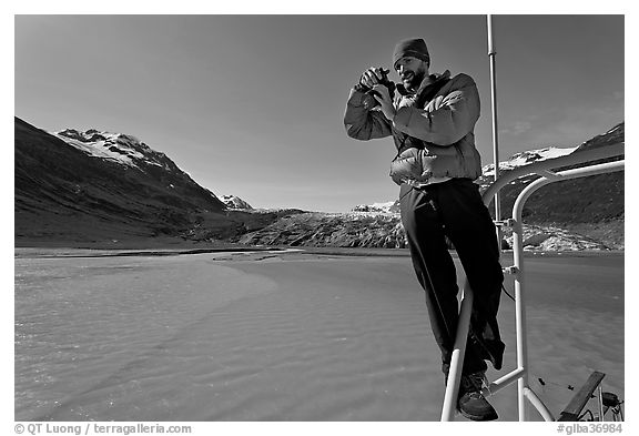 Photographer perched on boat with Reid Glacier behind. Glacier Bay National Park, Alaska, USA.