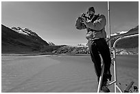 Photographer perched on boat with Reid Glacier behind. Glacier Bay National Park, Alaska, USA. (black and white)