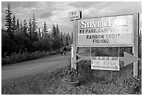 Sign and couple walking on McCarthy road near Silver Lake. Wrangell-St Elias National Park, Alaska, USA. (black and white)