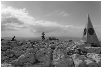 Hiker sitting on Guadalupe Peak summit with cairn and monument. Guadalupe Mountains National Park, Texas, USA. (black and white)