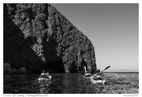 Kayakers paddling in kelp at base of sea cliff, Santa Cruz Island. Channel Islands National Park (black and white)