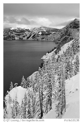 Cliffs, conifer trees, and lake in winter with cloudy skies. Crater Lake National Park (black and white)