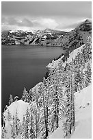 Cliffs, conifer trees, and lake in winter with cloudy skies. Crater Lake National Park, Oregon, USA. (black and white)