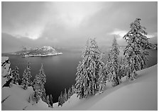 Snowy trees and lake with low clouds colored by sunset. Crater Lake National Park, Oregon, USA. (black and white)