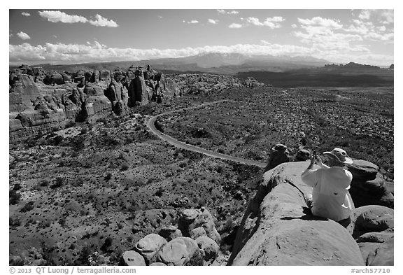 Tourist taking picture from top of fin. Arches National Park, Utah, USA.