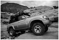 Expedition vehicle driving over rock ledge, Teapot Canyon. Canyonlands National Park, Utah, USA. (black and white)