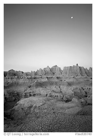 Mud cracks, badlands, and moon at dawn. Badlands National Park, South Dakota, USA.