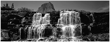 Waterfall flowing over dark rock and peak. Glacier National Park (Panoramic black and white)