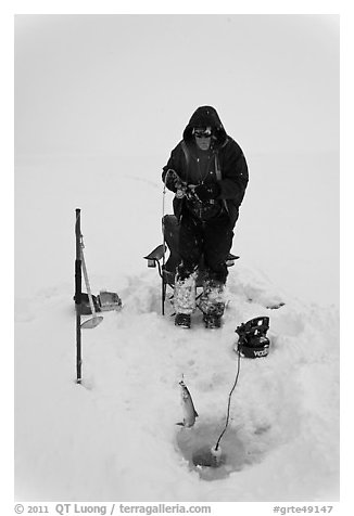 Man catching fish through hole in Jackson Lake ice. Grand Teton National Park, Wyoming, USA.