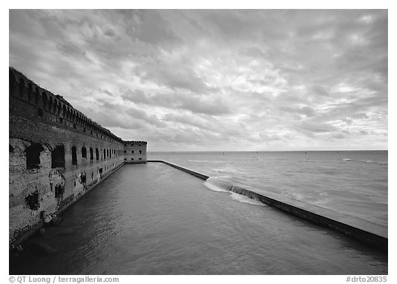 Fort Jefferson brick rampart and moat with wave over seawall, cloudy weather. Dry Tortugas National Park, Florida, USA.