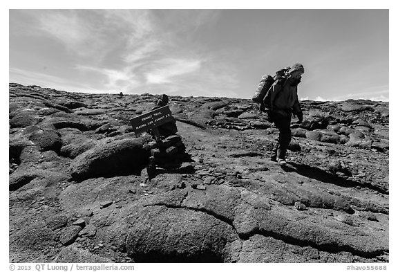 Hiker descending from Mauna Loa summit next to sign. Hawaii Volcanoes National Park (black and white)