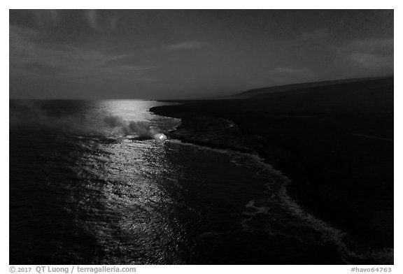 Aerial view of coastline with distant lava ocean entry and moonlight reflections at night. Hawaii Volcanoes National Park (black and white)
