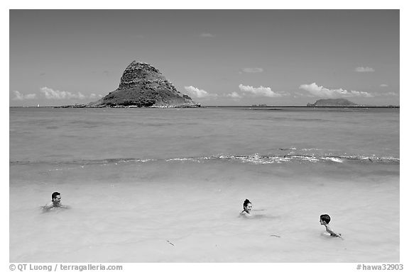 Family in the waters of Kualoa Park with Chinaman's Hat in the background. Oahu island, Hawaii, USA (black and white)