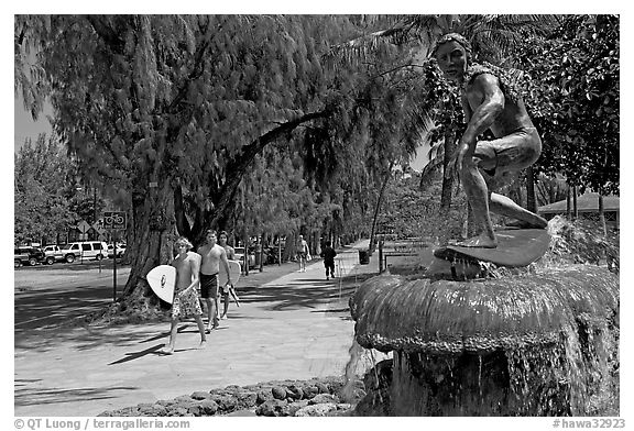 Young men carring surfboards next to statue of surfer, Kapiolani Park. Waikiki, Honolulu, Oahu island, Hawaii, USA